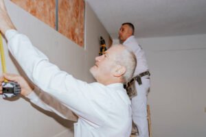 Two drywall installation contractors near Kendall FL working together on a wall, with tools and materials nearby in a residential space