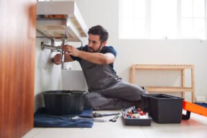 A plumber repairing a sink in a bathroom, performing plumbing repairs in Homestead FL with tools in hand.